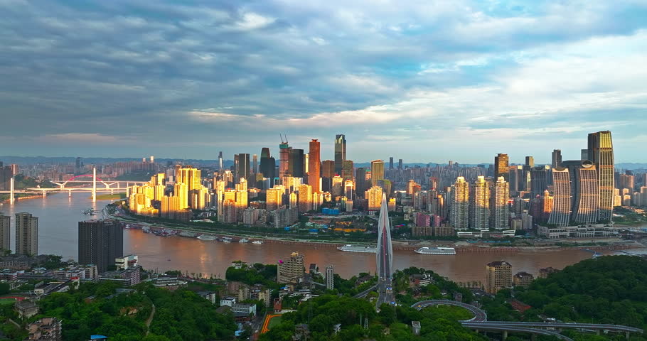 Aerial shot of Chongqing cityscape with modern skyscrapers and bridge crossing the river under dramatic sunrise clouds in China. Business and urban development concept.