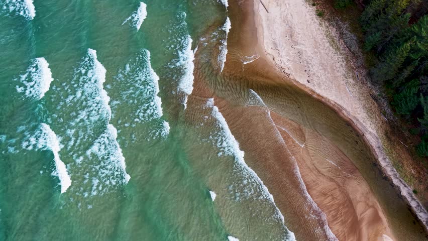 Aerial view of waves crashing along a sandy forested beach on the shores of Lake Superior in Michigan’s Upper Peninsula