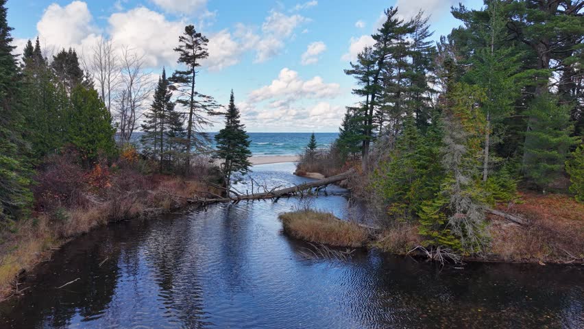 Peaceful aerial view of a forest-lined river inlet leading out to Lake Superior on a bright day in Michigan’s Upper Peninsula