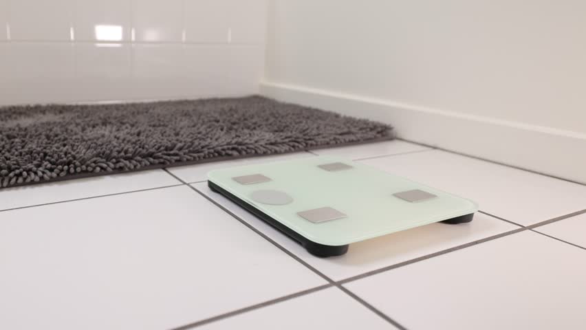 Woman checking her weight by stepping onto a bathroom scale.