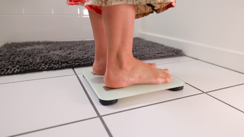 Woman checking her weight by stepping onto a bathroom scale.