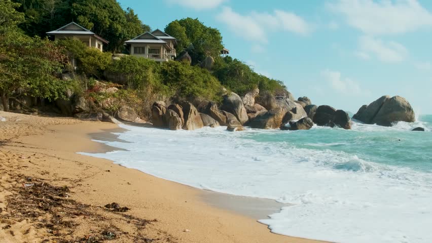 Man tourist walking on tropical beach with golden sand, turquoise water, rocky coastline with lush greenery and seaside villas. Male traveler on Coral cove sandy beach on Koh Samui island, Thailand