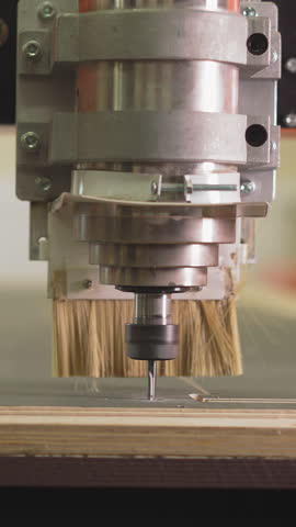 Wood lathe machine cuts out line in plywood sheet in woodwork shop closeup. Thin rotating drill processes timber while sawdust flies out slow motion