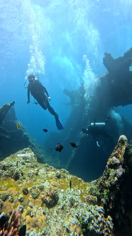 Scuba divers enjoying ocean adventure dive with tropical fish and coral exploring Ship Wreck in Bali Indonesia