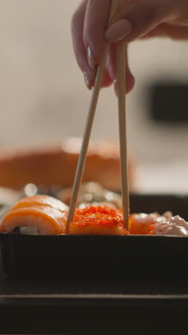 Woman hand takes delicious sushi roll with chopsticks in restaurant closeup. Lady enjoys Asian food for dinner slow motion. Luxury lifestyle