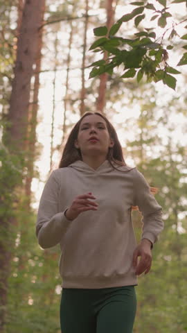 Female runner jogging across forest at morning dawn. Young woman enjoys cardio activity surrounded by dense trees. Active morning routine to shape body