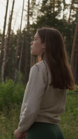Lonely woman stands in middle of forest. Sad lady thinks about meaning of existence walking in wild environment at sunset in evening. Devastation and depression