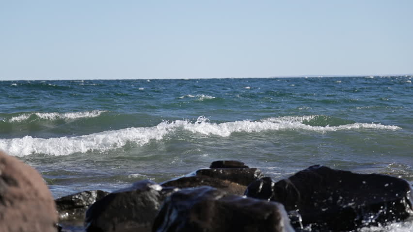 Big slow motion waves rolling into rocky shore in early evening with seagull flying through the sky, Lake Superior, Duluth, Minnesota, United States