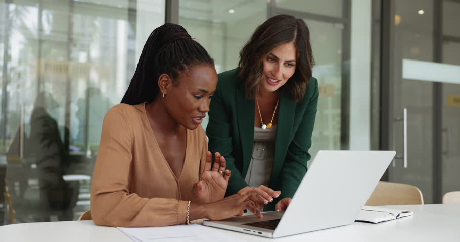 Young Latin business woman giving professional help, assistance to African colleague, showing web service, online product on laptop, typing, explaining application work