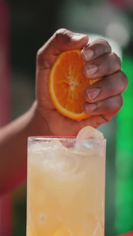 Barman squeezes orange half into cocktail in bar closeup. African American barkeeper adds fresh citrus ingredient to drink in nightclub. Party beverage