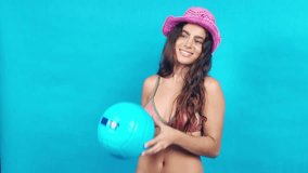 Beautiful young woman wearing a pink hat and bikini playing with a beach ball on a blue background - Powered by Shutterstock - Get 15% off with code: PIKWIZARD15