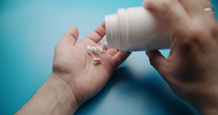 Close-up slow motion shot of white pills being poured into a hand against a solid blue background. Medical and pharmaceutical concept with clean composition.