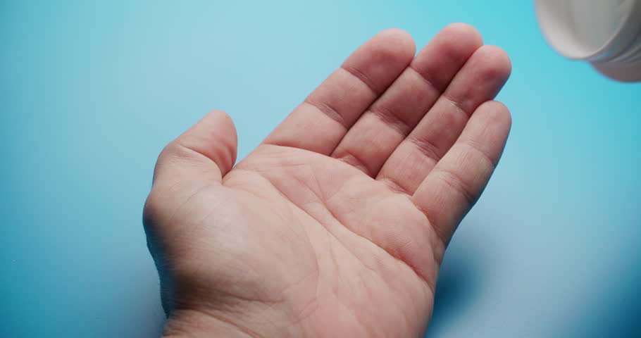Close-up slow motion shot of white pills being poured into a hand against a solid blue background. Medical and pharmaceutical concept with clean composition.