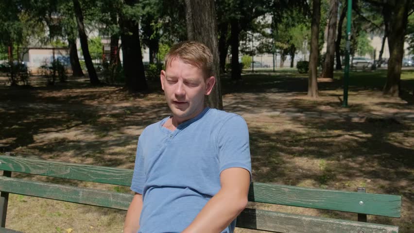 Man suffering from heat wave, guy with heatstroke. Caucasian male presses bottle of water to face to cool off. Exhausted tired overheated man. Sunstroke at summer hot weather