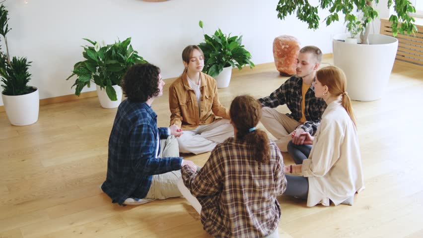 Multiracial Group of individuals practicing mindfulness meditation in a bright indoor space surrounded by plants on a calm afternoon