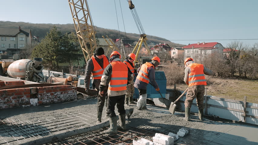 Construction workers pouring concrete on site, team in orange vests working outdoors.