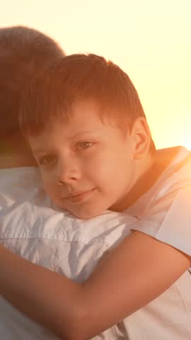 Boy hugs father with arms on street. Child son hugs dad on sunny meadow. Father loves his son, happy hugs of child dad. Family walk in nature. Family, dad son walk together in sun park. Kid boy parent
