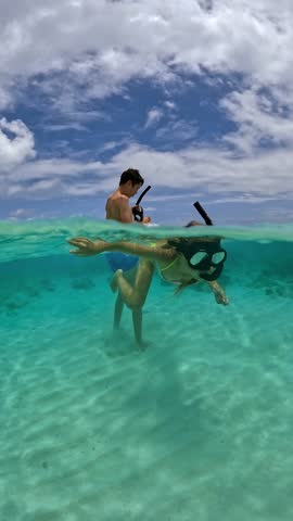 Two children snorkel underwater in Bora Bora, interacting near the sandy ocean floor, with clear water and coral visible.