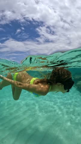 Two children snorkel underwater in Bora Bora, interacting near the sandy ocean floor, with clear water and coral visible.