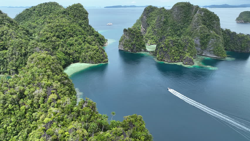 A small boat cruises through a maze of islands in Misool, Raja Ampat, Indonesia. This area is known as the heart of marine biodiversity and is a popular destination for diving and snorkeling.