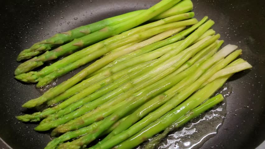 Fresh asparagus being gently fried in a black skillet, capturing the rustic charm of homemade, healthy meals.

