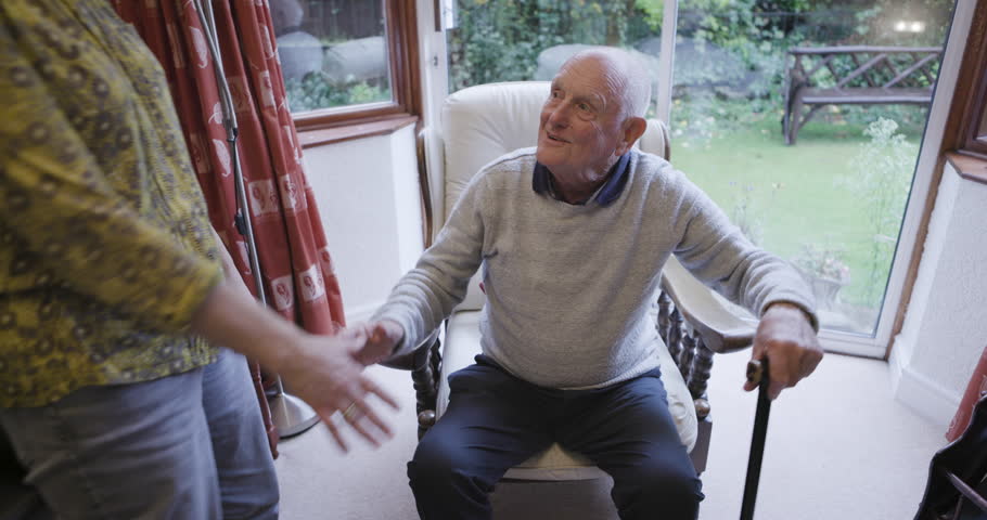 Disability, help and senior couple holding hands for walking, balance and support in their home together. Love, trust and elderly woman helping man in wheelchair, standing and hold hand while bonding