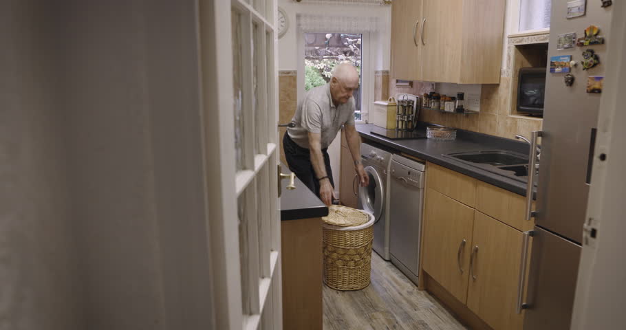 Senior man, dirty laundry and washing machine in kitchen, home and cleaning alone with technology for hygiene. Elderly gentleman, washing clothes and clean in apartment, house or flat for cleanliness