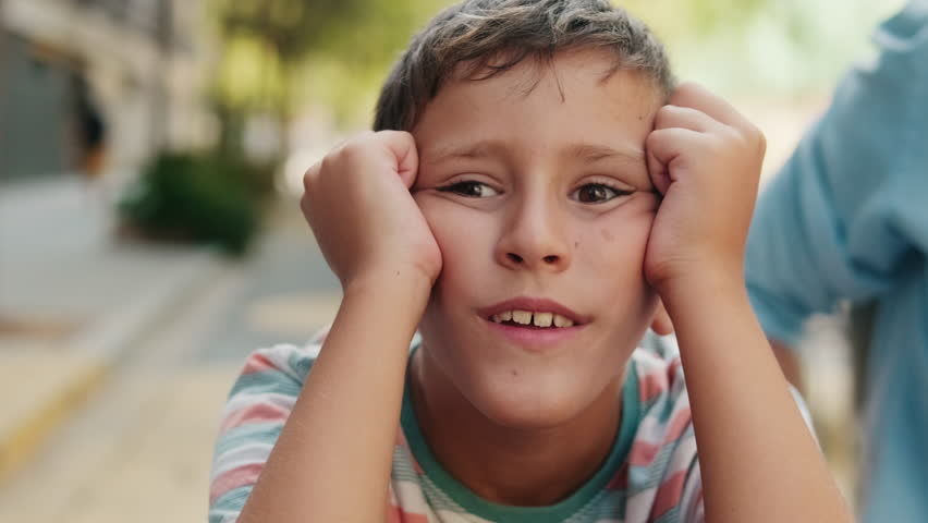 A young boy with his hands on his cheeks makes a funny face. He looks bored and restless while waiting.