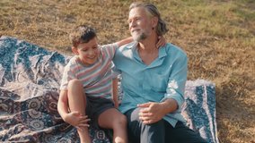 Grandfather and grandson are sitting on a blanket on the grass and talking. They are smiling and laughing together and they share a hug. - Powered by Shutterstock - Get 15% off with code: PIKWIZARD15