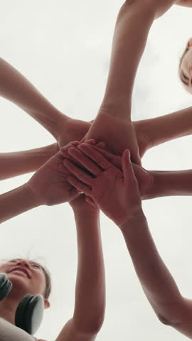 Vertical video, Four diverse female friends put their hands together and raise them up in the air, outdoors and smiling. A great representation of fitness, teamwork, and friendship.
