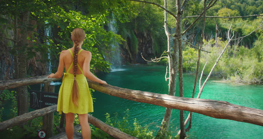 Woman watches turquoise waterfall lake in Plitvice National Park Croatia forest