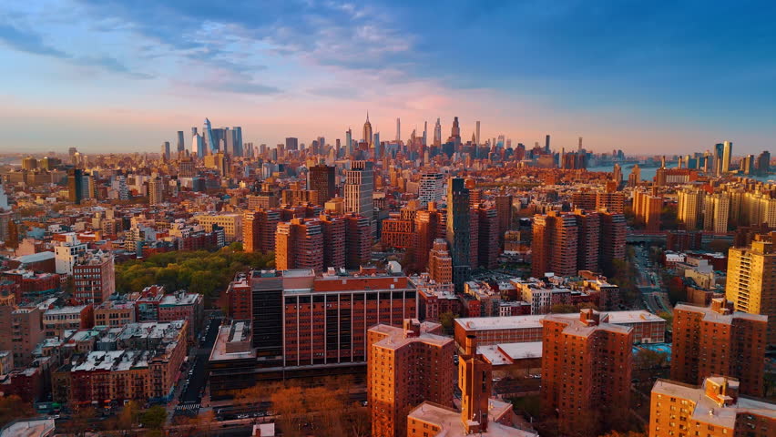 Varied urban landscape of New York in the orange light of setting sun. Skyscraper skyline at backdrop. Aerial view.