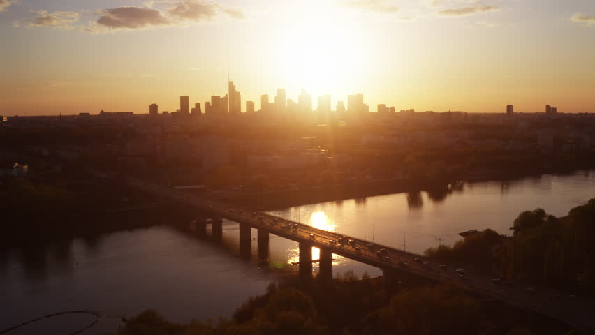 Aerial panoramic view Warsaw city. Cinematic drone shot cityscape downtown skyline, high rise skyscrapers modern architecture buildings on horizon backlit with orange sunset light, bridge over river