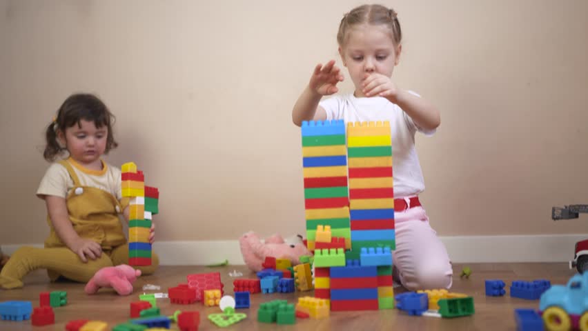 Two little girls playing with blocks. A group of children play with toys in a kindergarten. Lifestyle constructors build a kindergarten together. Two young girls playing with building blocks.