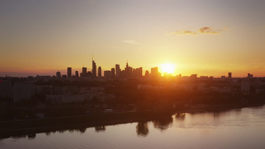 Aerial panoramic view Warsaw city. Cinematic drone shot cityscape downtown skyline, high rise skyscrapers modern architecture buildings on horizon backlit with orange sunset light, bridge over river