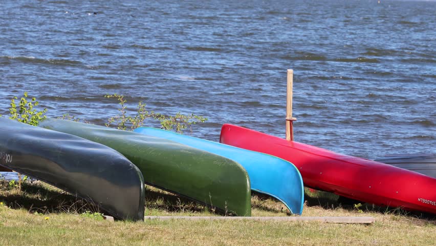 Hampetorp, Sweden A man walks on a beach on Lake Hjalmaren with upturned green, blue and red canoes. 