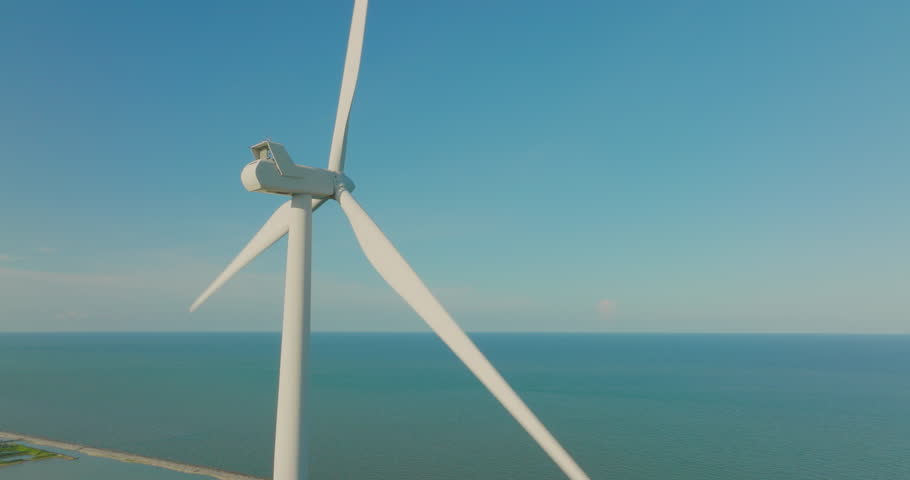 Aerial view orbiting the field of wind turbine for energy production in blue sky. Drone flies over a windmill farm generating clean renewable energy for sustainable development green ecological world.