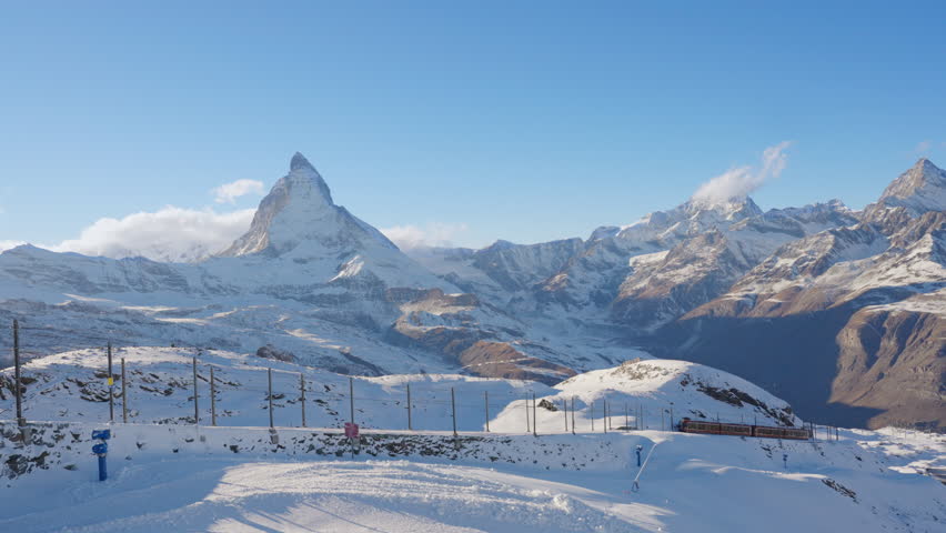 Gornergrat bahn railway running towards summit station with Matterhorn mountain peak background in Zermatt on a sunny winter day. Swiss Alps, Switzerland travel journey trip. 4K Static Shot.