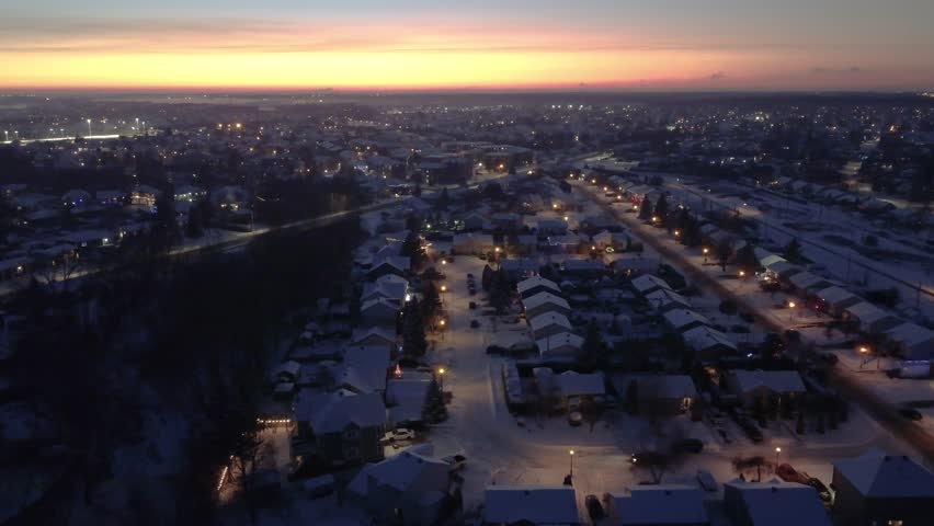 Snowy Suburban Neighborhood at at blue hour with sunset colors in the horizon during winter. Aerial view