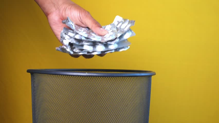 A hand is throwing away expired medicine packet into a trash can.