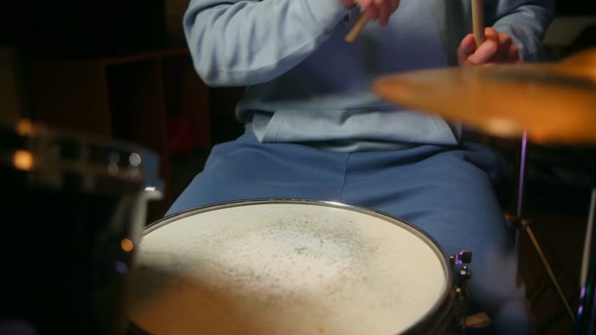 Drummer passionately plays drum set with dynamic stick movements, showcasing rhythmic skills and musical energy. Close-up captures intense focus and physicality of live percussion performance.