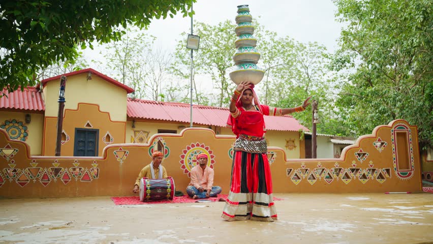 Rural artist dances balancing clay pots on head outdoor, Lady folk dancer performing her heritage groove at village, Duo turbaned man sits playing music in local ceremony, Tribal enjoys their festive