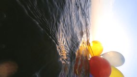 Bunch of airy multi-colored balloons swing on the waves of sea on sunny summer day. The sun shining through balloons. Slow motion Vertical. Many colored small balloons tied together float on surface - Powered by Shutterstock - Get 15% off with code: PIKWIZARD15
