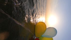 Bunch of airy multi-colored balloons swing on the waves of sea on sunny summer day. The sun shining through balloons. Slow motion Vertical. Many colored small balloons tied together float on surface - Powered by Shutterstock - Get 15% off with code: PIKWIZARD15