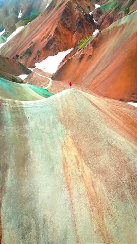 Vertical aerial: Hiker overlooks stunning colorful Landmannalaugar mountains, Iceland. Unique volcanic highlands, vibrant travel adventure backdrop. Ideal for social media stories.