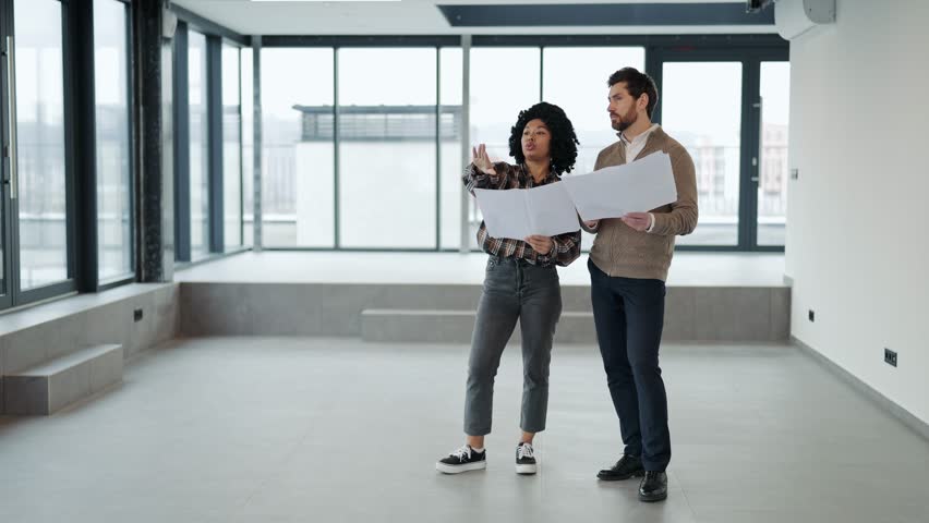 International agreement on cooperation in commercial real estate investment. Husband and wife discuss blueprints in modern office space. Smartly dressed, they experience emotions of focus - Powered by Shutterstock - Get 15% off with code: PIKWIZARD15