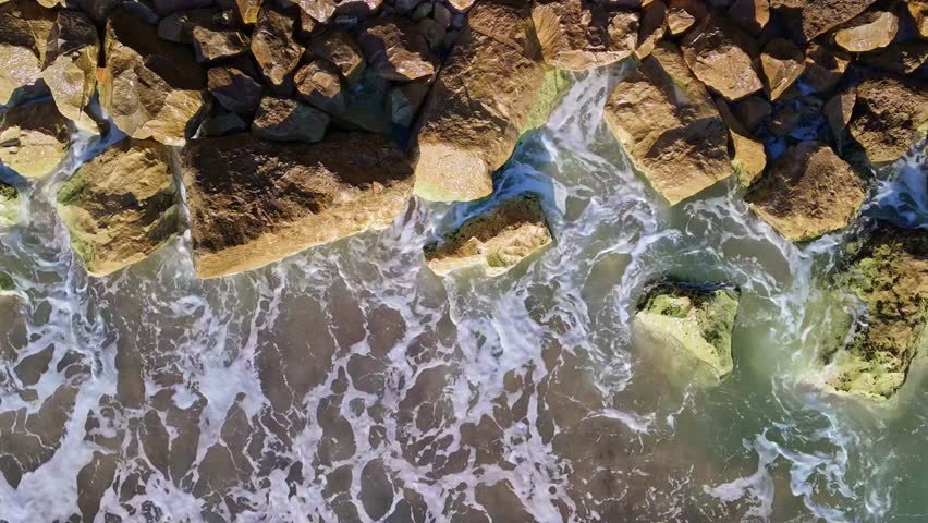 Dynamic rocky shoreline in Bulgaria, with turbulent waves crashing onto large, algae-covered rocks. Ideal for showcasing dramatic coastal landscapes and nature