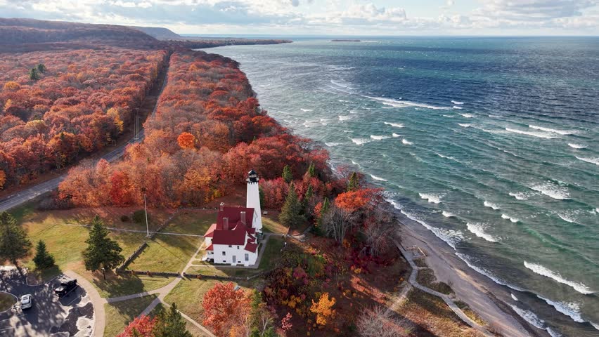 Dramatic aerial drone shot of a coastal lighthouse surrounded by vibrant fall foliage on the shores of Lake Superior in Michigan’s Upper Peninsula