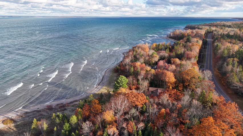 Aerial drone footage of a forest-lined road hugging the rugged Lake Superior shoreline during peak autumn color in Michigan’s Upper Peninsula