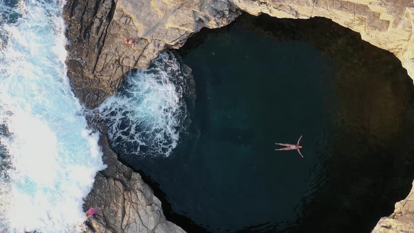 Above aerial slow motion view of a girl swimming and swimming in Giola lagoon, natural pool near the sea, in Thassos island, Greece